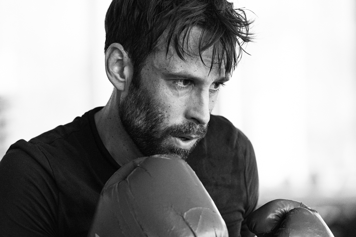 Ein Boxer im Ringside Gym, Berlin, Lichtenberg. Er trägt blaue Boxhandschuhe und wirkt erschöpft.