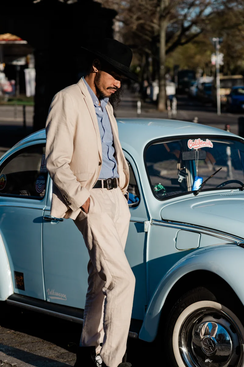 Ein Schauspielerporträtfoto eines Mannes in einem hellen Anzug, der neben einem klassischen Volkswagen Beetle steht. Aufgenommen in Berlin Kreuzberg